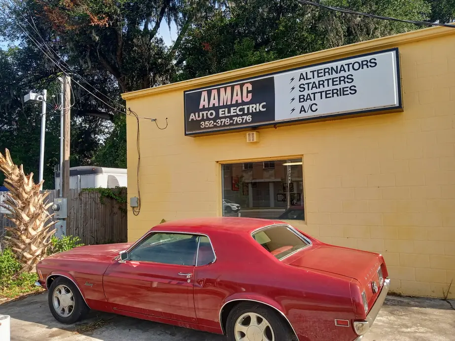 The AAMAC Auto Electric sign reading Alternators, Starters, Batteries, A/C and 352-378-7676 on the yellow building, with a red classic Mustang parked out front